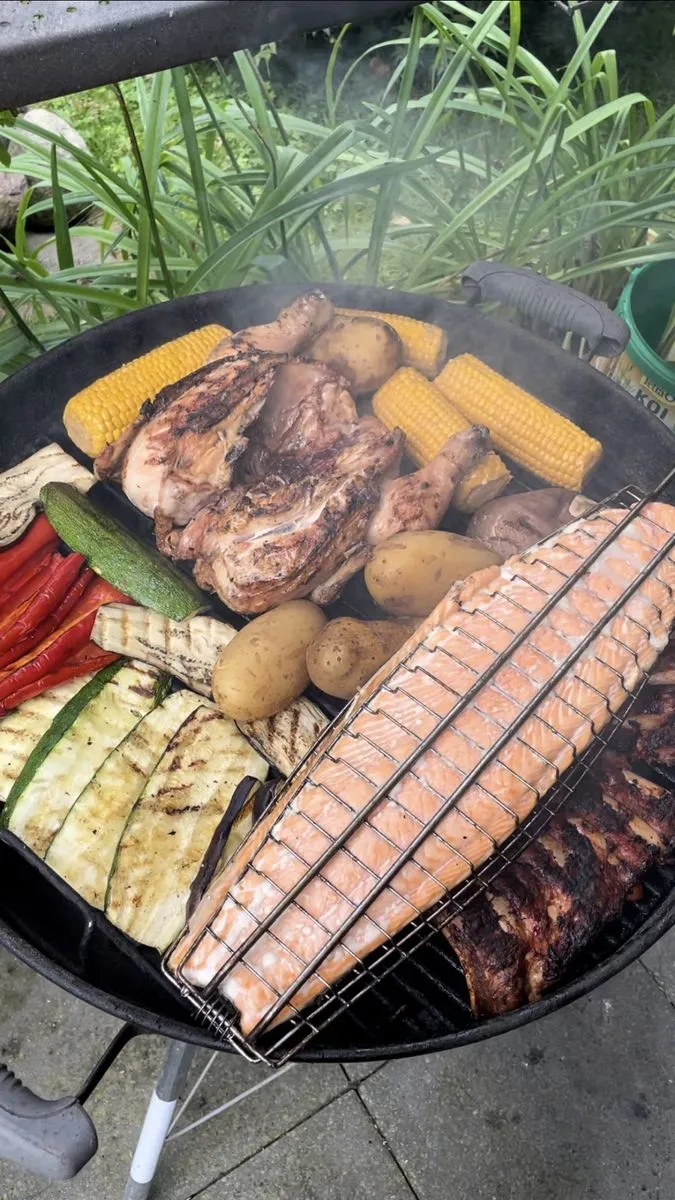 Voll belegter Kugelgrill mit Maiskolben, Steaks, Kartoffeln und einer Lachsseite im Fischkorb