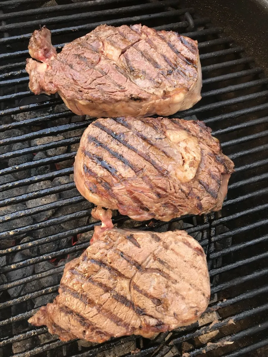 Drei dicke Steaks mit Grillstreifen auf dem Rost